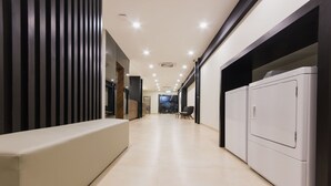 Um corredor moderno com um banco, uma máquina de lavar e uma porta que dá para outro cômodo.