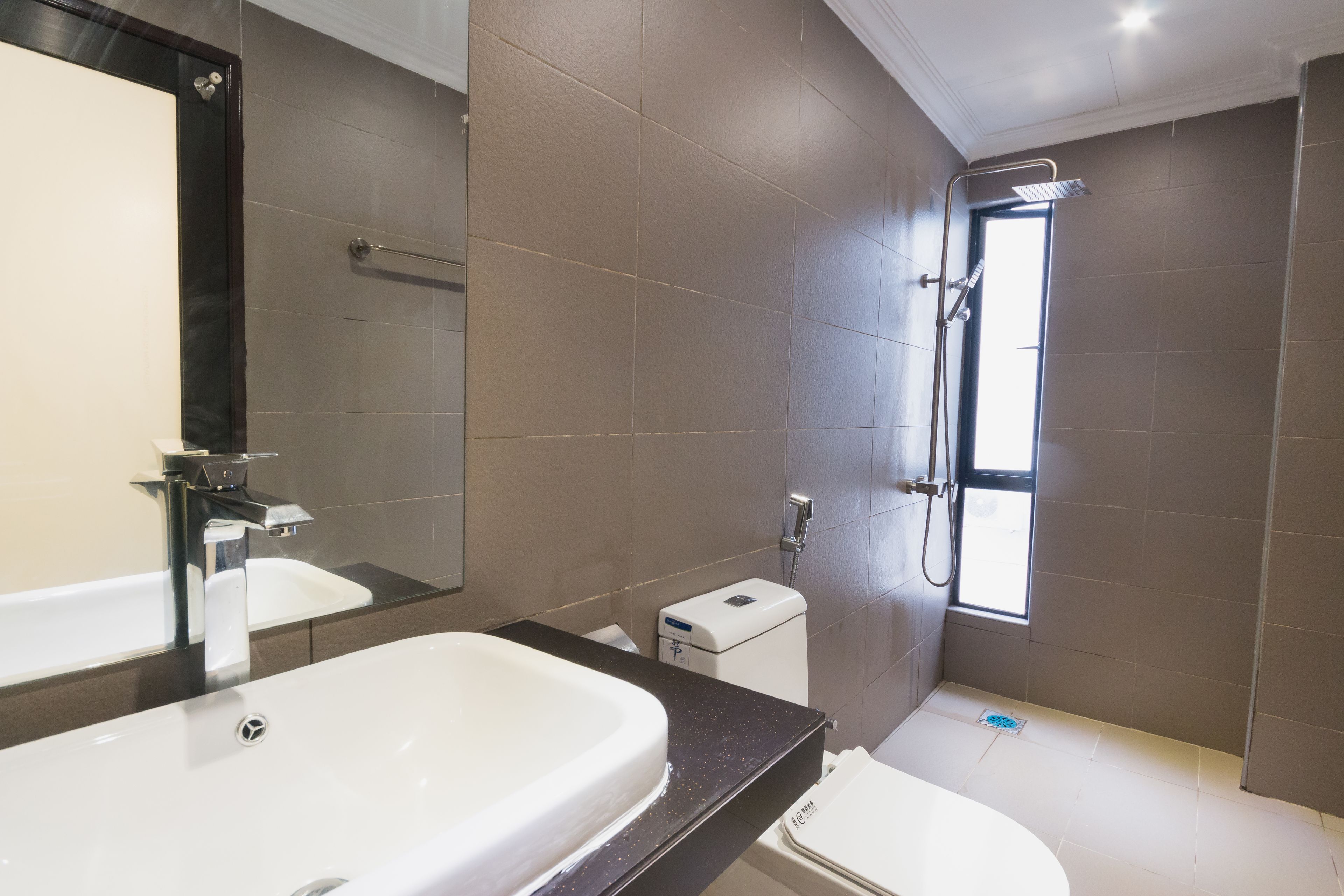 Un baño moderno con un espejo grande, un lavabo blanco, un inodoro y una zona de ducha.