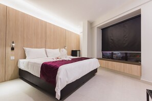 Une chambre moderne avec un grand lit, des murs recouverts de panneaux en bois, un téléviseur intégré et une fenêtre donnant sur la ville.