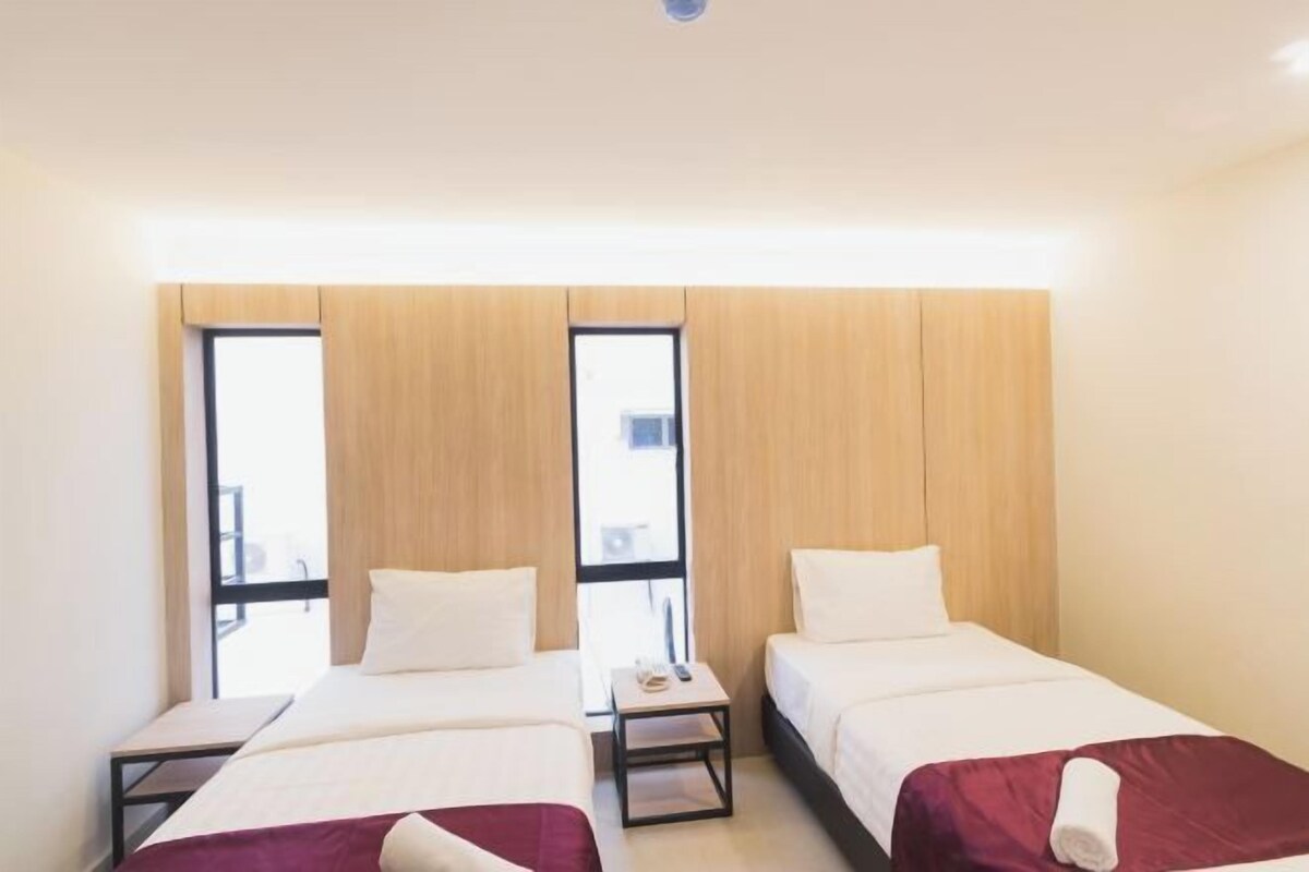 Une chambre d’hôtel avec deux lits simples, une petite table et une fenêtre donnant sur un paysage agréable.