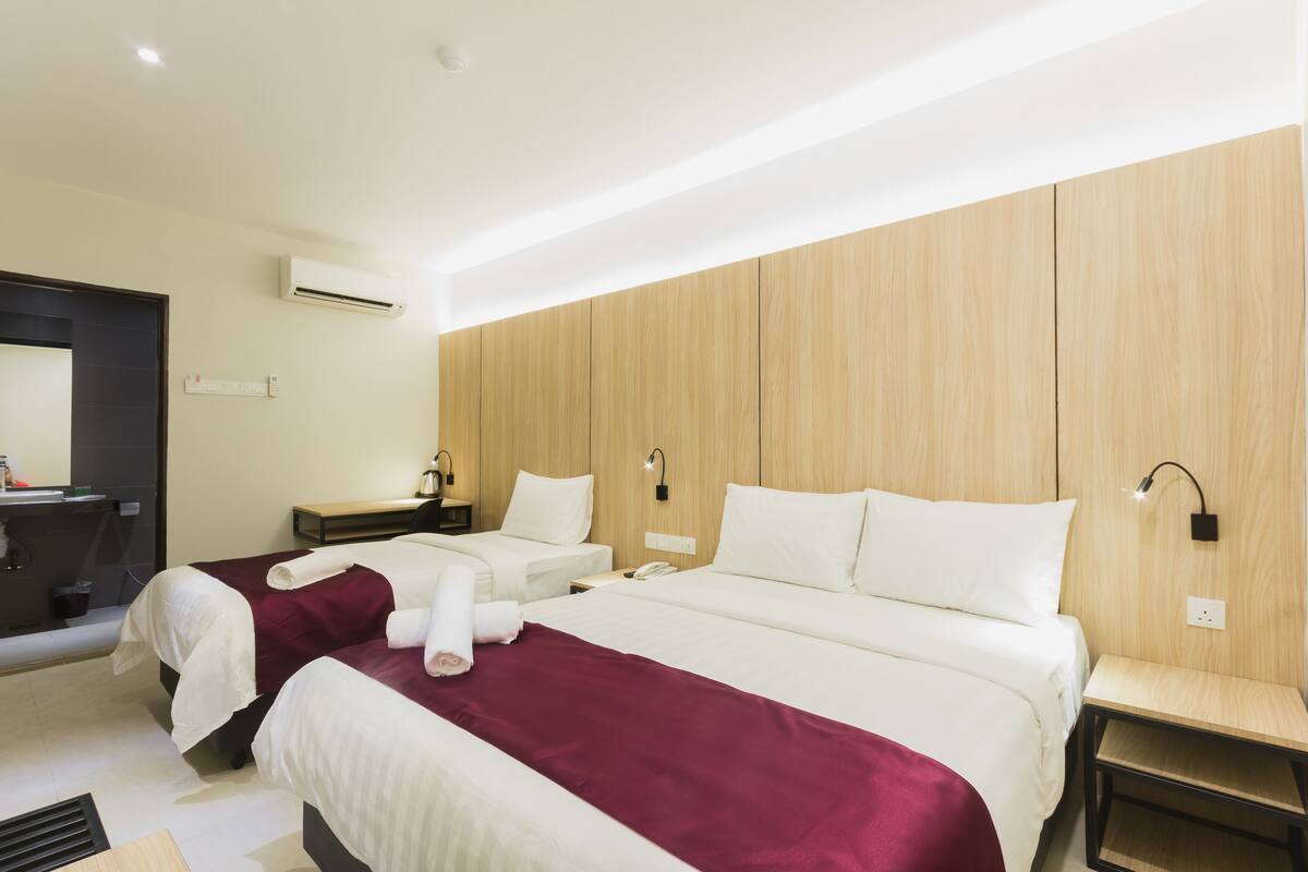 A hotel room with two beds, a wooden panel wall, a small desk, and a mirror.
