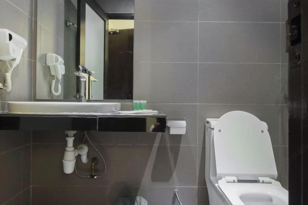 Une salle de bain moderne avec des toilettes blanches, un lavabo avec un miroir et un sèche-cheveux fixé au mur.