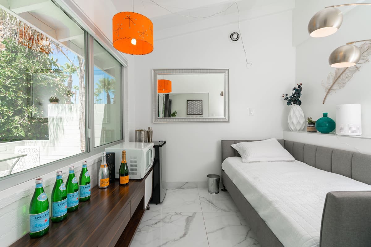 A modern bedroom with a bed, a nightstand, a mirror, and a window with bottles on the sill.