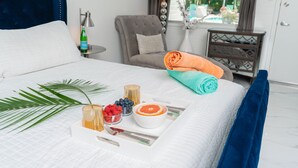 A neatly made bed with a white quilt, a blue headboard, and a tray with fruits and a bowl of orange slices. - BelleVue Oasis-Palm Springs - Adults Only (Palm Springs)