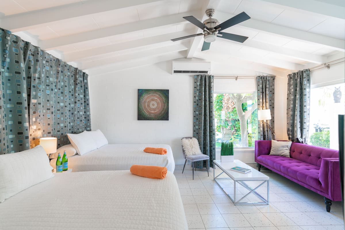 A hotel room with two beds, a purple sofa, a coffee table, a chair, and a ceiling fan.