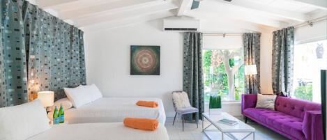 A hotel room with two beds, a purple sofa, a coffee table, a chair, and a ceiling fan.