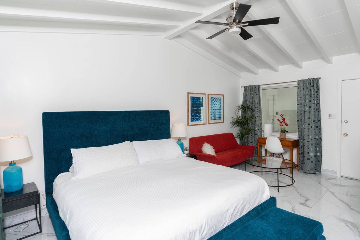 A modern bedroom with a large bed, a ceiling fan, a red armchair, and a small table with a lamp.