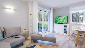 Uma sala moderna com sofá, repouso para os pés, televisão de tela plana e área de jantar com mesa e cadeiras.