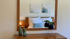 A bedroom with a wooden headboard, a bedside table with a potted plant, and two framed artworks on the wall. - Charming Apartment with Private Garden & Pool (Vilamoura)