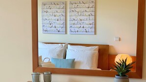 A bedroom with a bed, pillows, a bedside table with jars, a lamp, and wall art of birds. - Charming Apartment with Private Garden & Pool (Vilamoura)