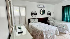 A bedroom with two beds, a bedside table, a mirror, and a window with blinds.