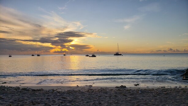 A beach with boats in the water and a clear sky.
