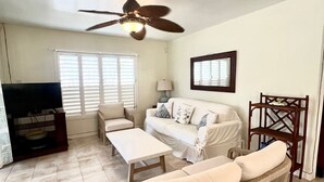 A living room with a sofa, coffee table, TV stand, and a ceiling fan.