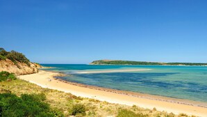 Una playa costera con aguas azules cristalinas, orillas de arena y un paisaje montañoso al fondo.