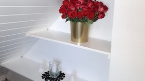 A white shelf with a gold vase containing red roses, a small glass container, and a decorative item.