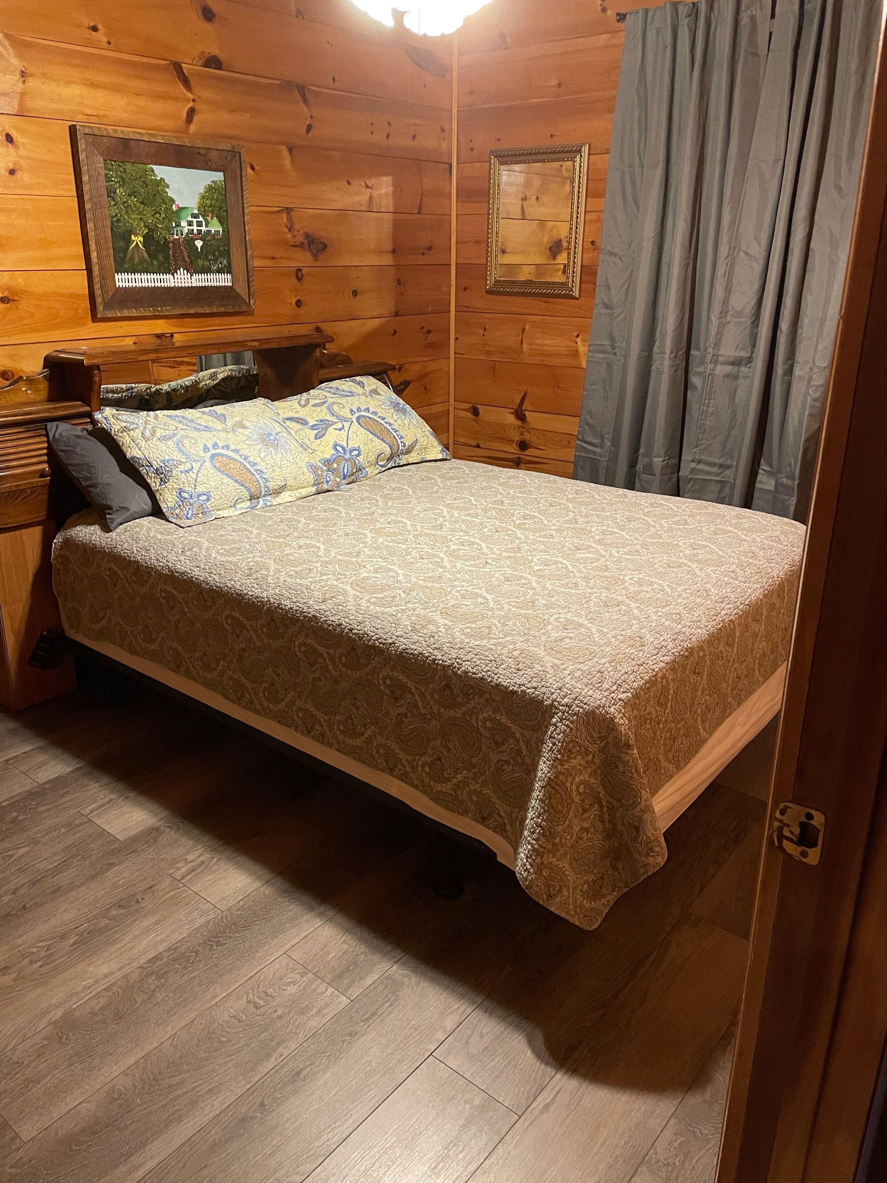Un dormitorio de cabaña de madera con cama, mesita de noche, cómoda y dos cuadros en la pared.