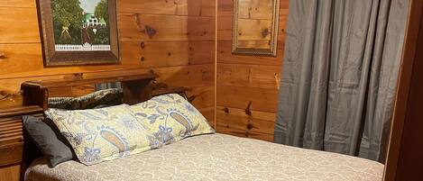 Un dormitorio de cabaña de madera con cama, mesita de noche, cómoda y dos cuadros en la pared.