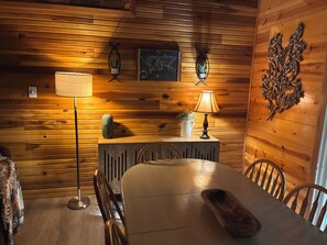 Une pièce aux murs lambrés, comprenant une table à manger, des chaises, une lampe, une plante et un élément décoratif mural.
