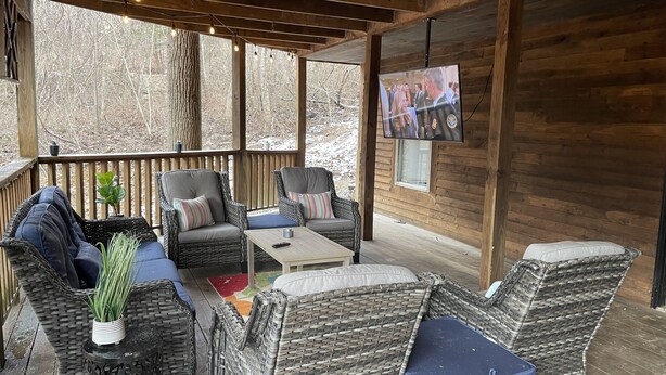 A covered outdoor seating area with wicker furniture, a television, and a wooden deck.