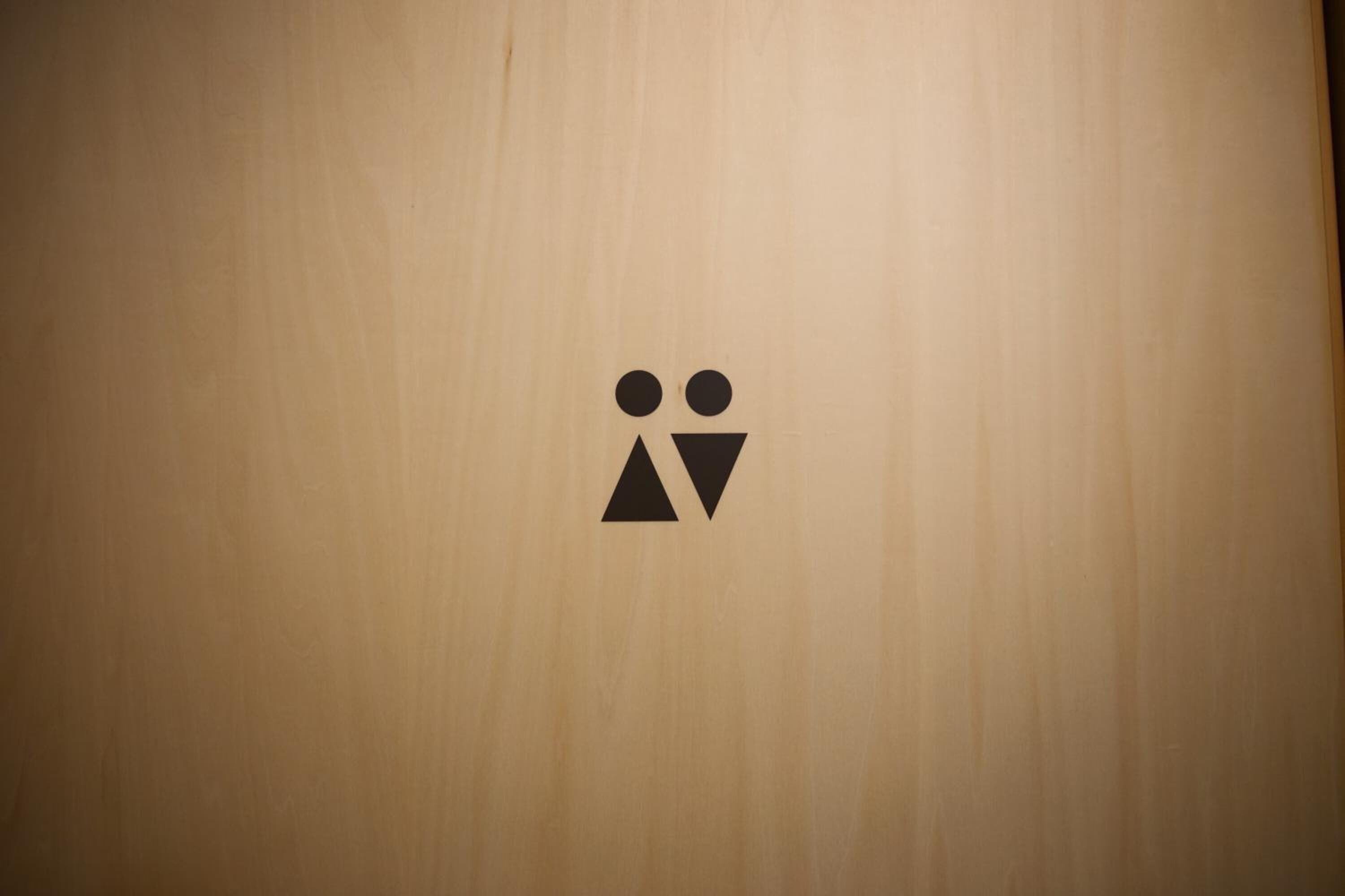 Un mur en bois orné d’un simple pictogramme noir représentant deux personnes et un triangle, qui indique probablement l’emplacement de toilettes ou la fonction spécifique d’une pièce.