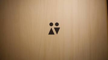 Un mur en bois orné d’un simple pictogramme noir représentant deux personnes et un triangle, qui indique probablement l’emplacement de toilettes ou la fonction spécifique d’une pièce.