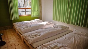 Habitación con tres camas individuales alineadas junto a la pared, suelo de madera y cortinas verdes en una ventana.