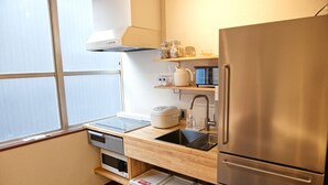 Una cocina compacta con un refrigerador de acero inoxidable, un lavamanos y un microondas. Hay gabinetes de almacenamiento debajo de la encimera y una ventana que proporciona luz natural.