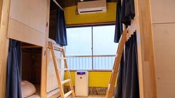 A dormitory room with bunk beds, a window, and an air conditioning unit.