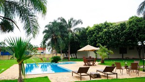 A swimming pool with lounge chairs and an umbrella, surrounded by lush greenery and palm trees. - Terras Hotel (Lucas do Rio Verde)