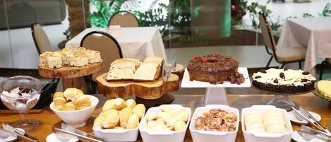 Une table de buffet proposant une variété d’aliments, notamment du pain, des pâtisseries et des desserts.