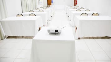 A conference room with rows of tables and chairs, a projector on the front table, and a door in the background.