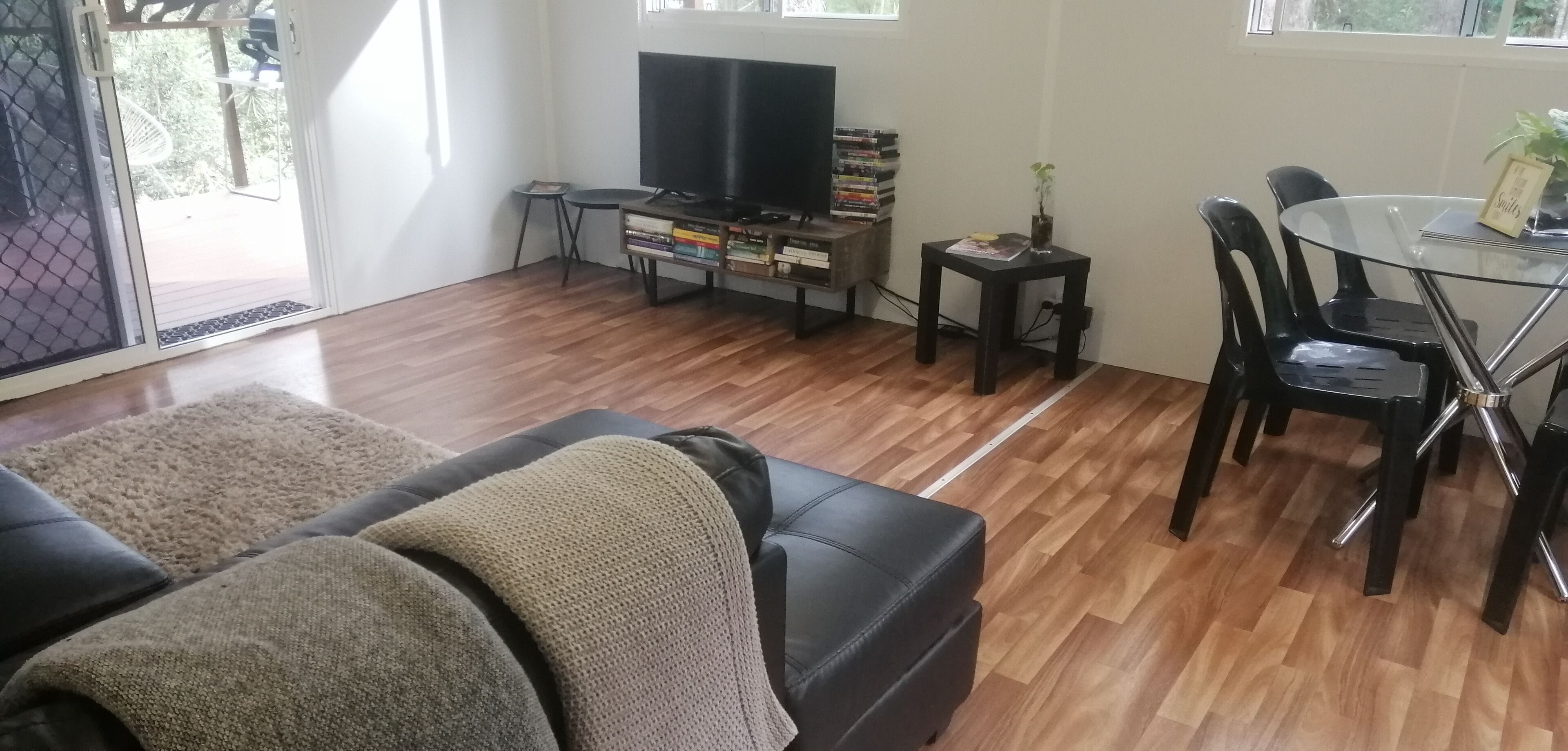 A living room with a black leather sofa, a glass coffee table, a TV, and a small side table with a plant.