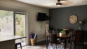 Uma área de refeições com mesa, cadeiras, um relógio e uma televisão na parede.