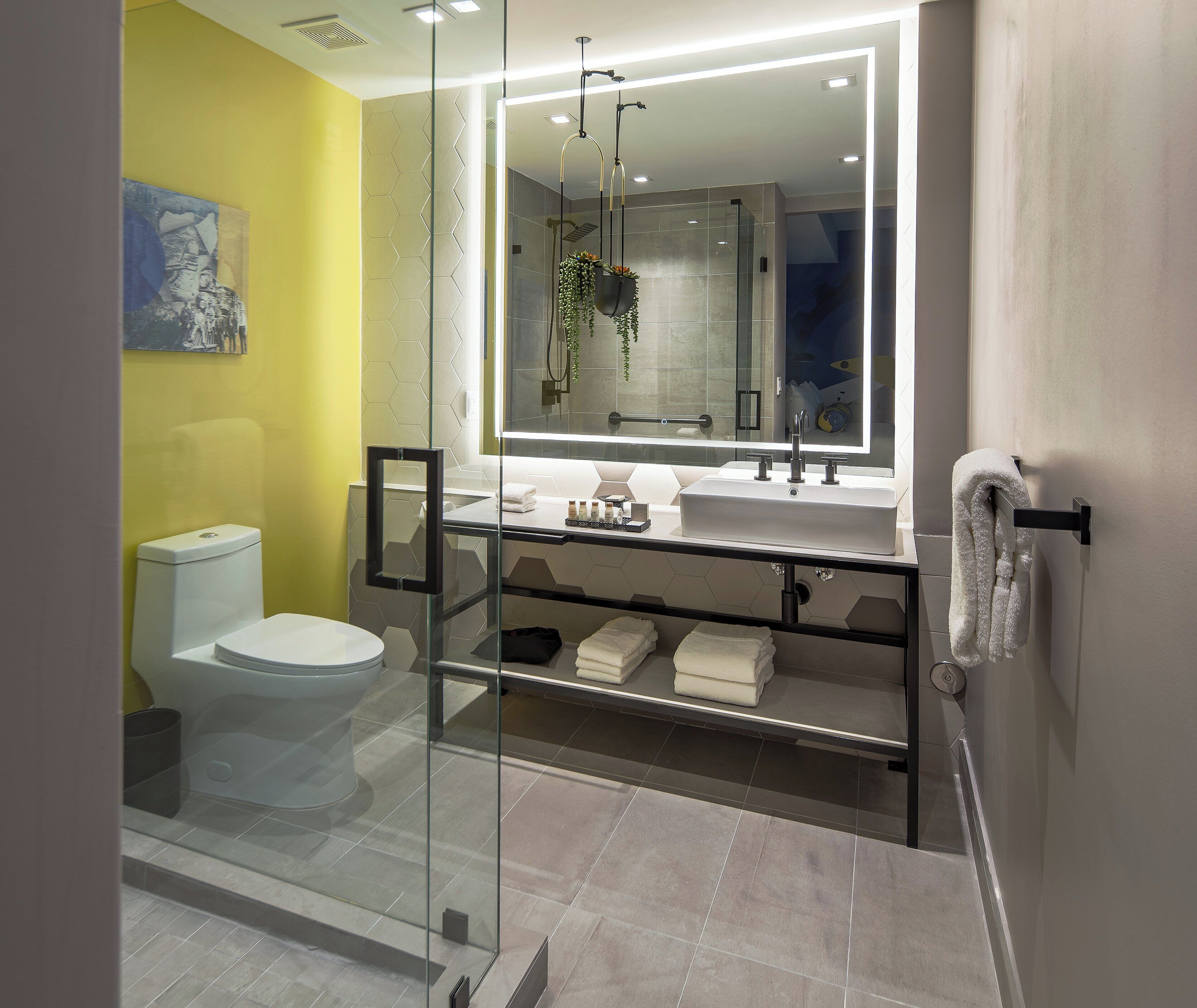 A modern bathroom with a glass shower enclosure, a white toilet, a large mirror, and a vanity with a sink and towel rack.