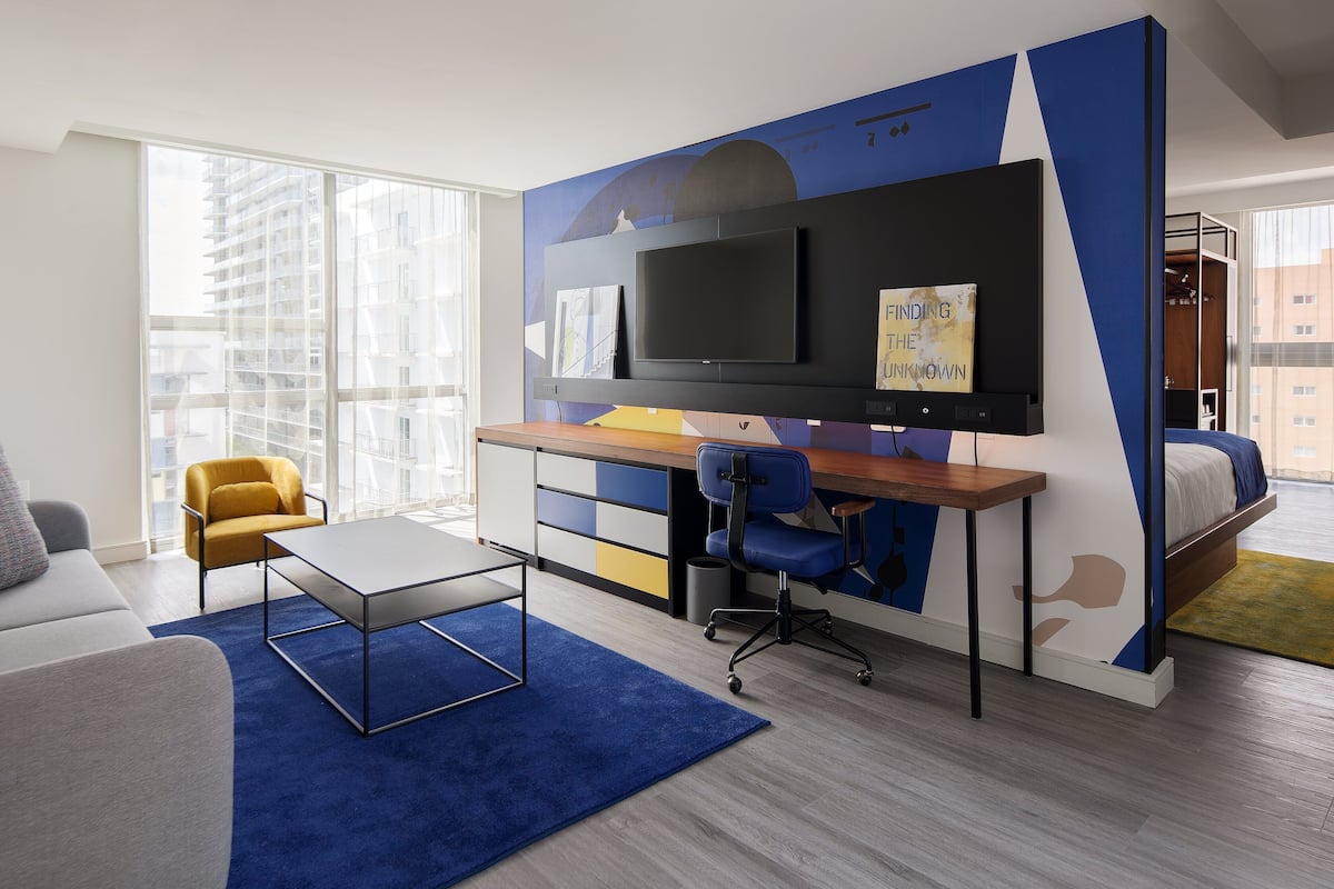 A modern hotel room with a desk, chair, and a bed.