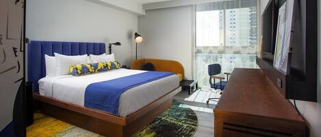Une chambre d’hôtel moderne dotée d’un grand lit, d’un bureau, d’une chaise, d’une télévision et d’une grande fenêtre donnant sur la ville.
