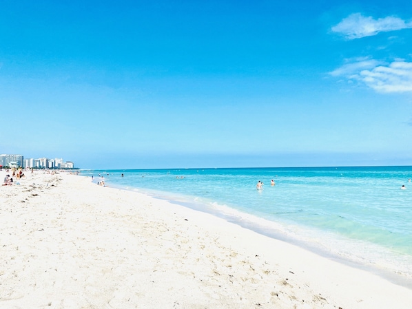 Uma praia com águas azuis cristalinas, areia branca e algumas pessoas nadando.