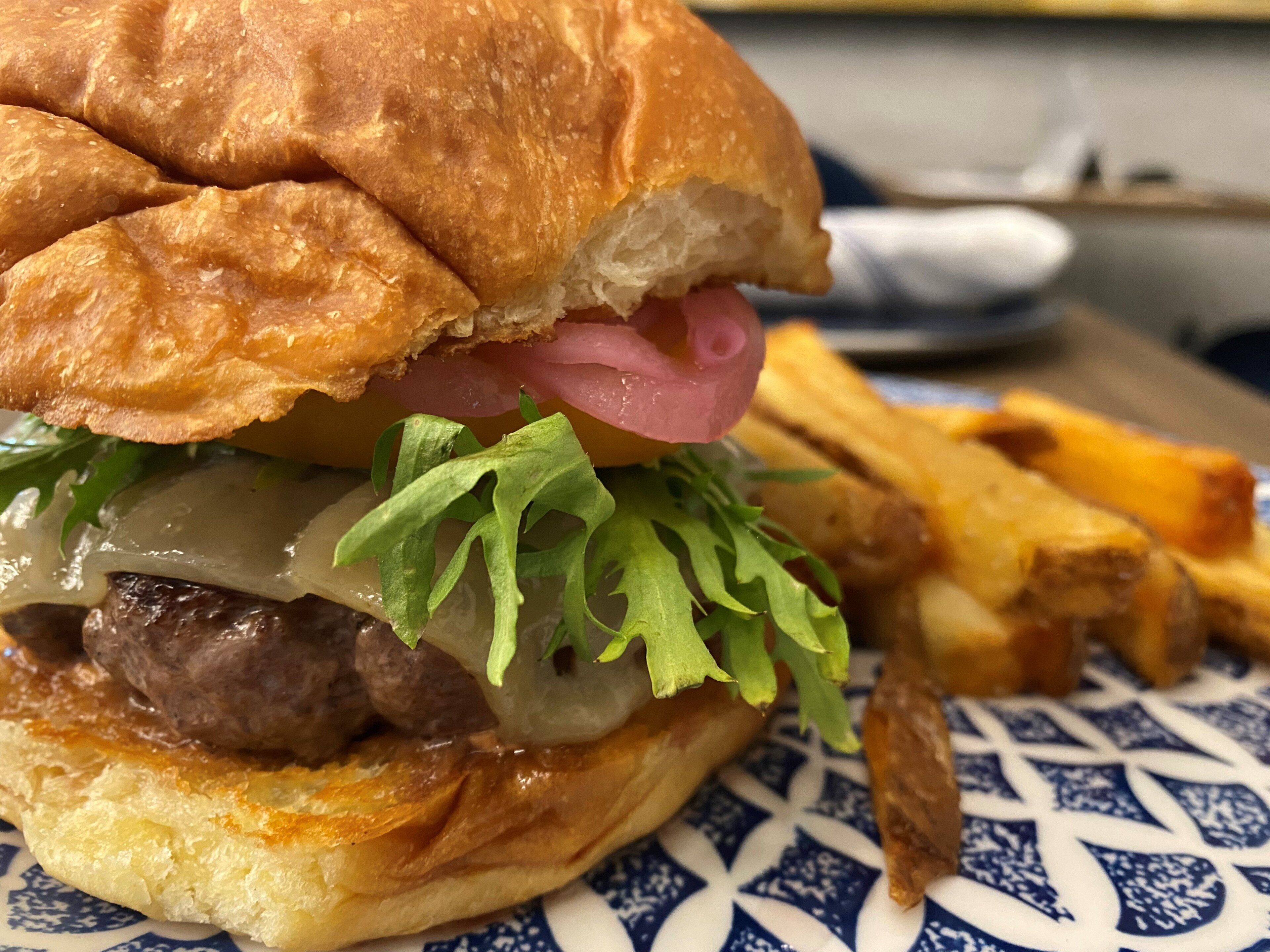 A sandwich with a bun, meat, cheese, lettuce, and onions.