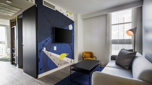A modern living room with a flat-screen TV mounted on a wall, a sofa with a cushion, a coffee table, and a lamp. - Hotel Indigo Miami Brickell by IHG (Miami)