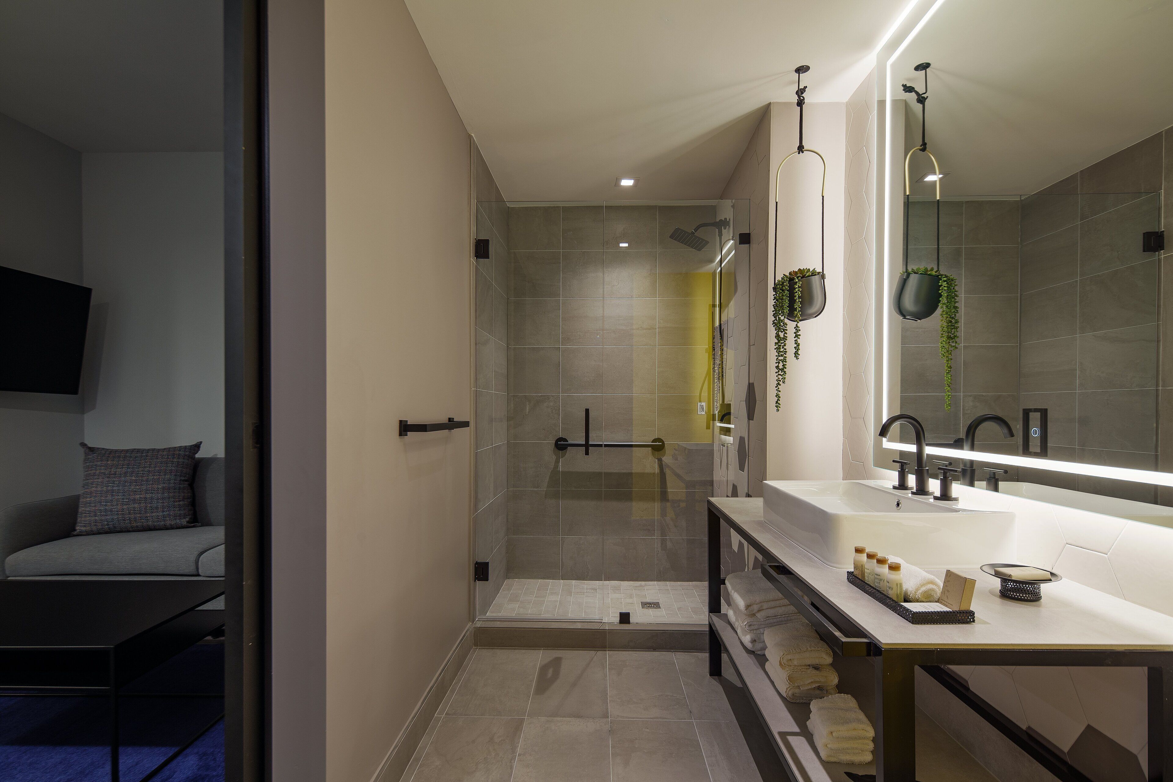 A modern bathroom with a glass-enclosed shower, a large mirror, and a vanity with toiletries.