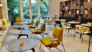 Ein moderner Loungebereich mit runden Tischen, gelben Sesseln und einem großen Bücherregal.