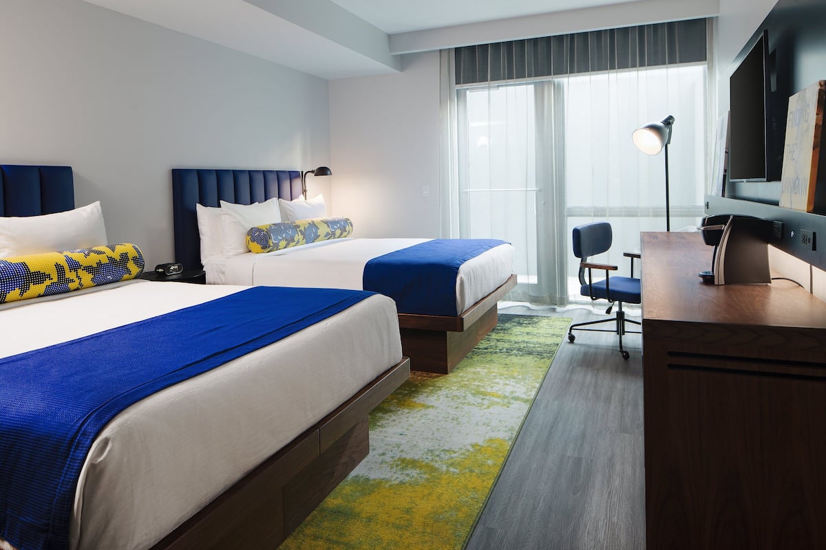 A hotel room with two beds, a desk, a chair, a television, and a large window.