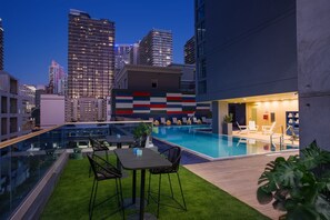 A rooftop pool area with a glass balustrade, outdoor seating, and a view of the city skyline at dusk. - Hotel Indigo Miami Brickell by IHG (Miami)