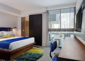 Quarto de hotel com cama, escrivaninha, cadeira, janela grande e vista para a cidade.