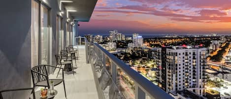 Un balcón con mobiliario exterior, con vistas a un paisaje urbano al atardecer.