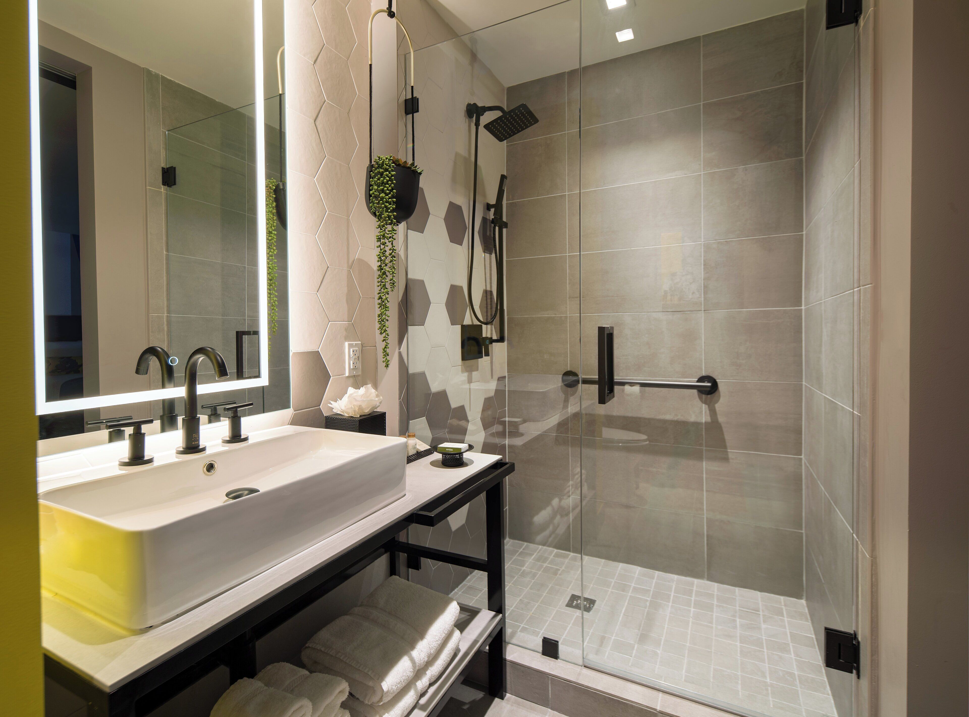 Un baño moderno con un espejo grande, lavamanos dobles, ducha con mampara de vidrio y un perchero para toallas.