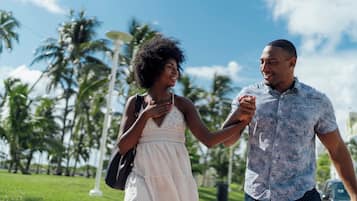 A couple walking hand in hand on a sunny day with palm trees in the background.