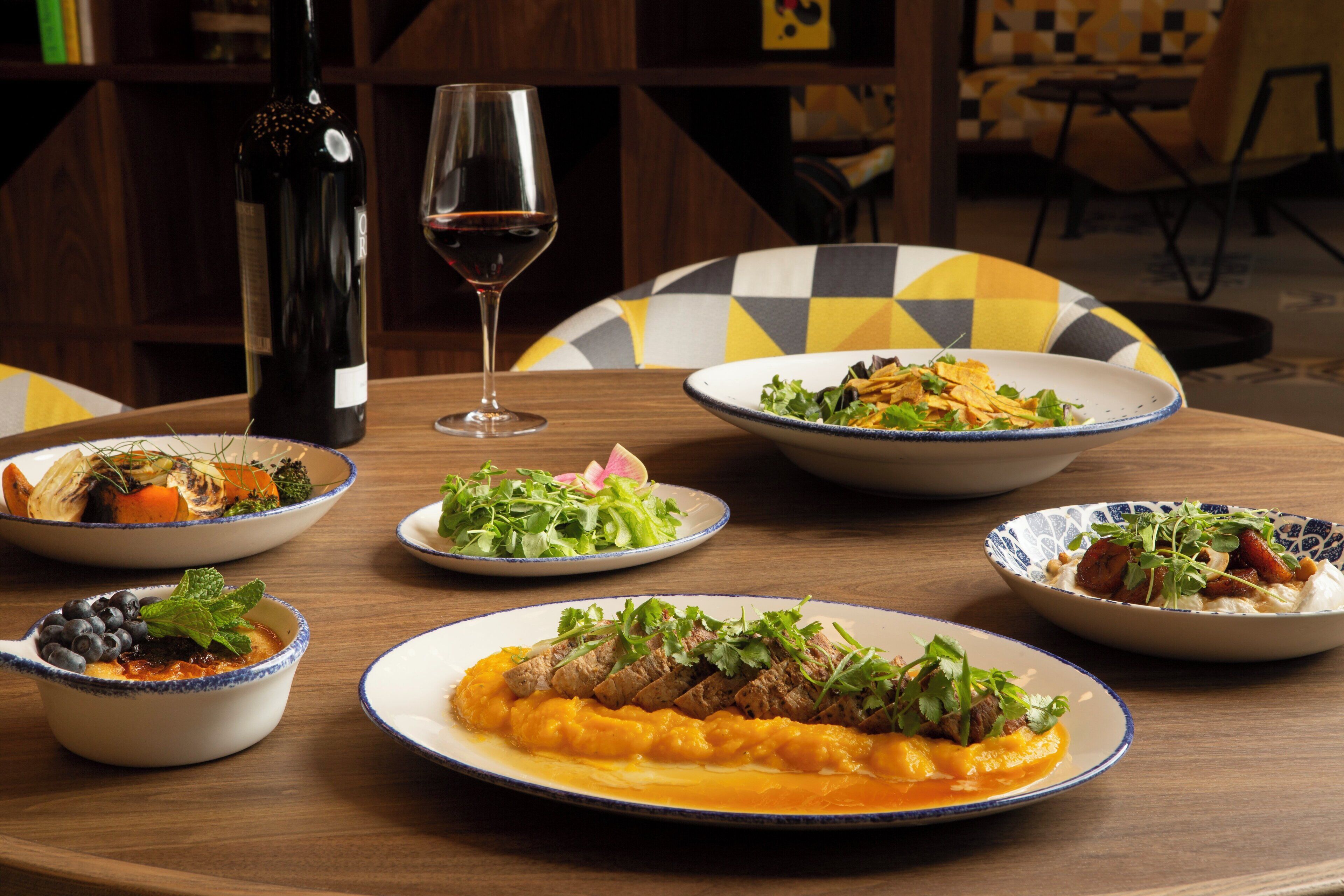 A round table with various dishes, a wine bottle, and a glass of wine.