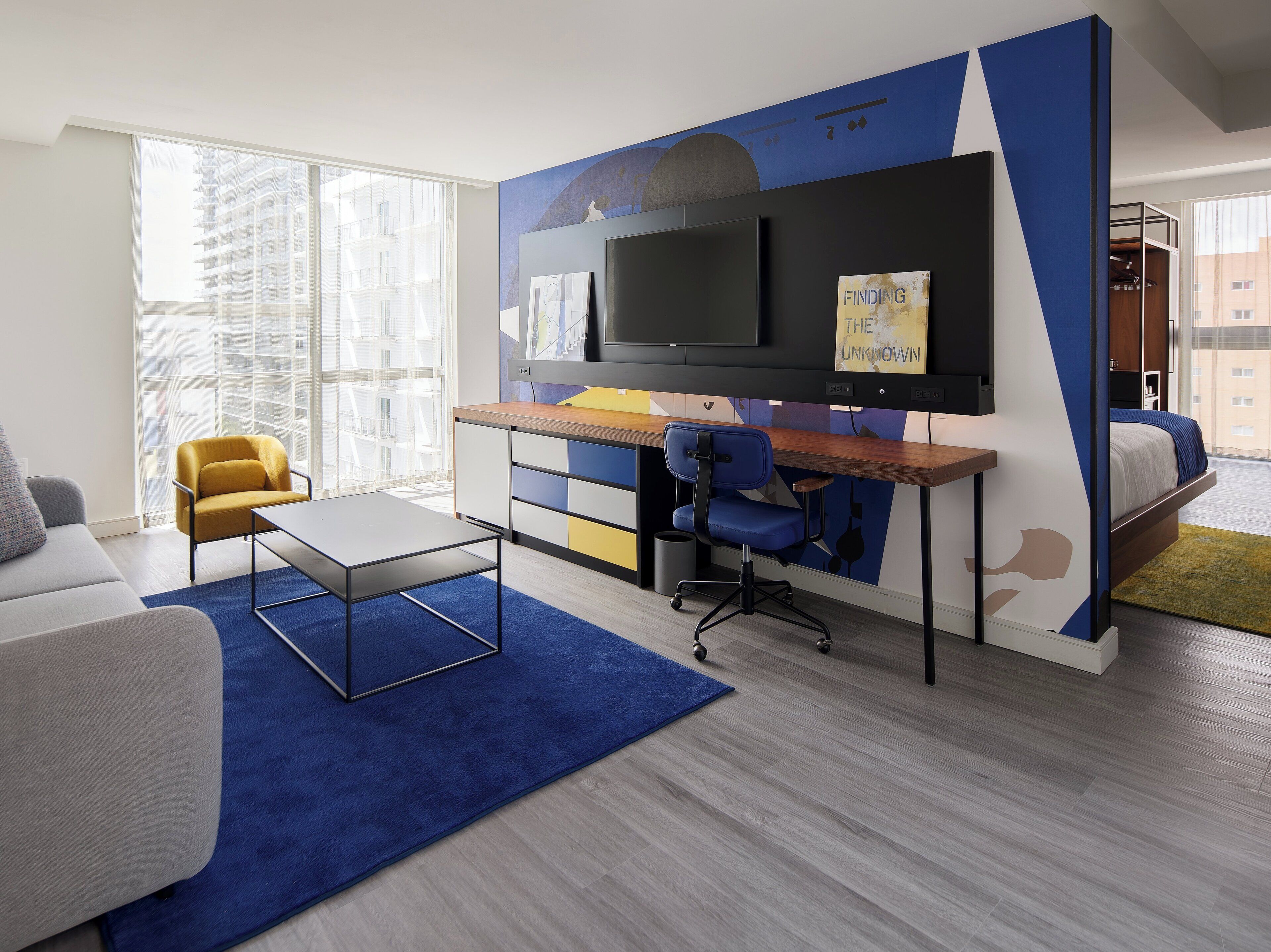 A modern hotel room with a desk, chair, sofa, and a bed.