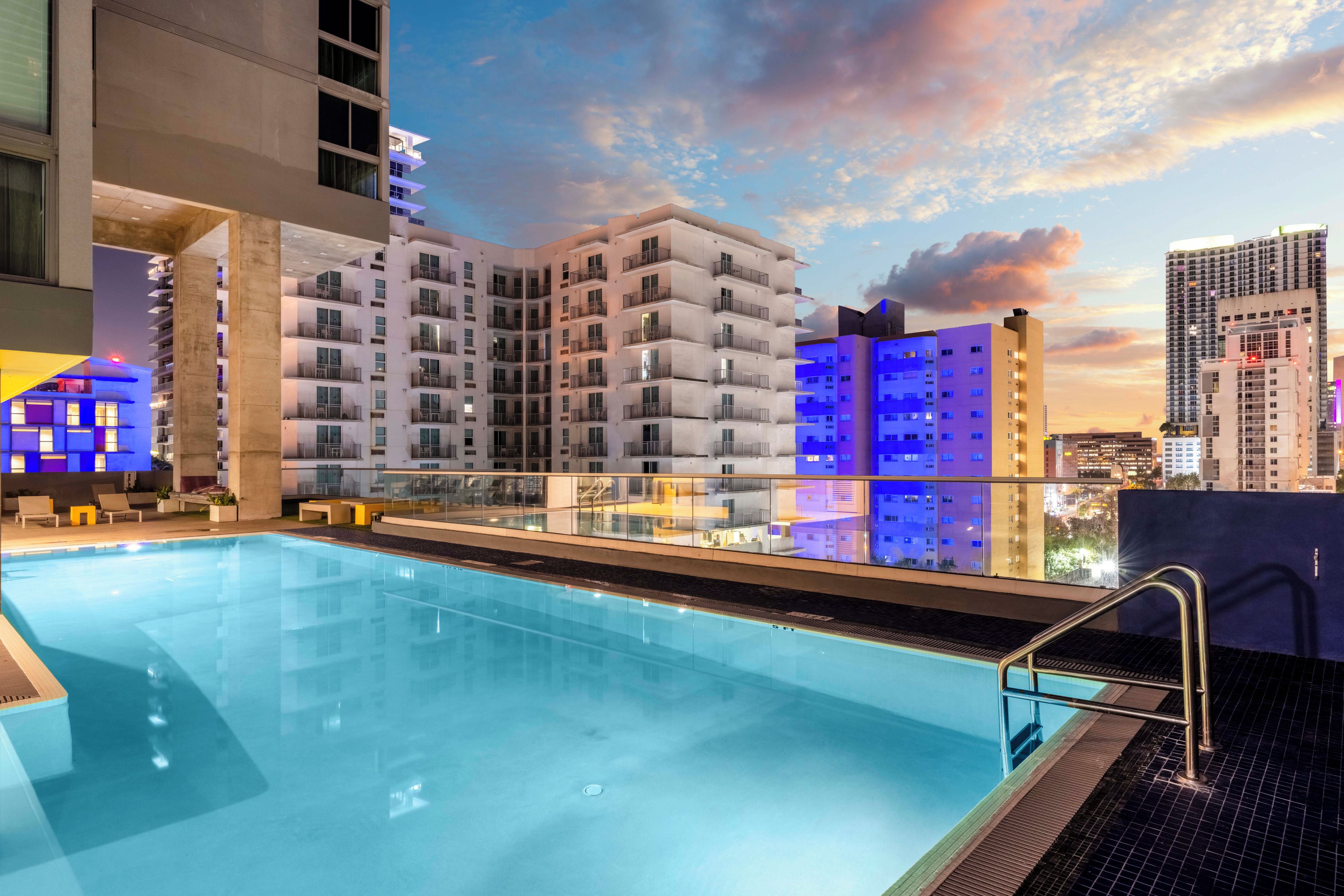 A rooftop pool with a glass balustrade, surrounded by high-rise buildings with balconies.